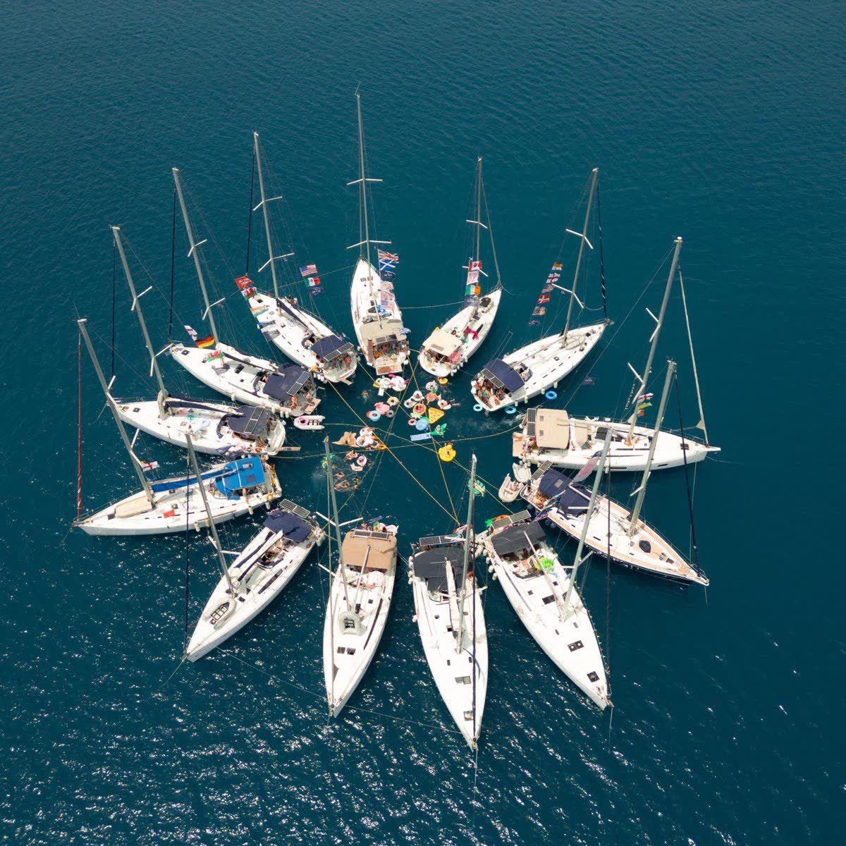Yachts rafted together in a fan seen from above, bows pointing out into deep blue water