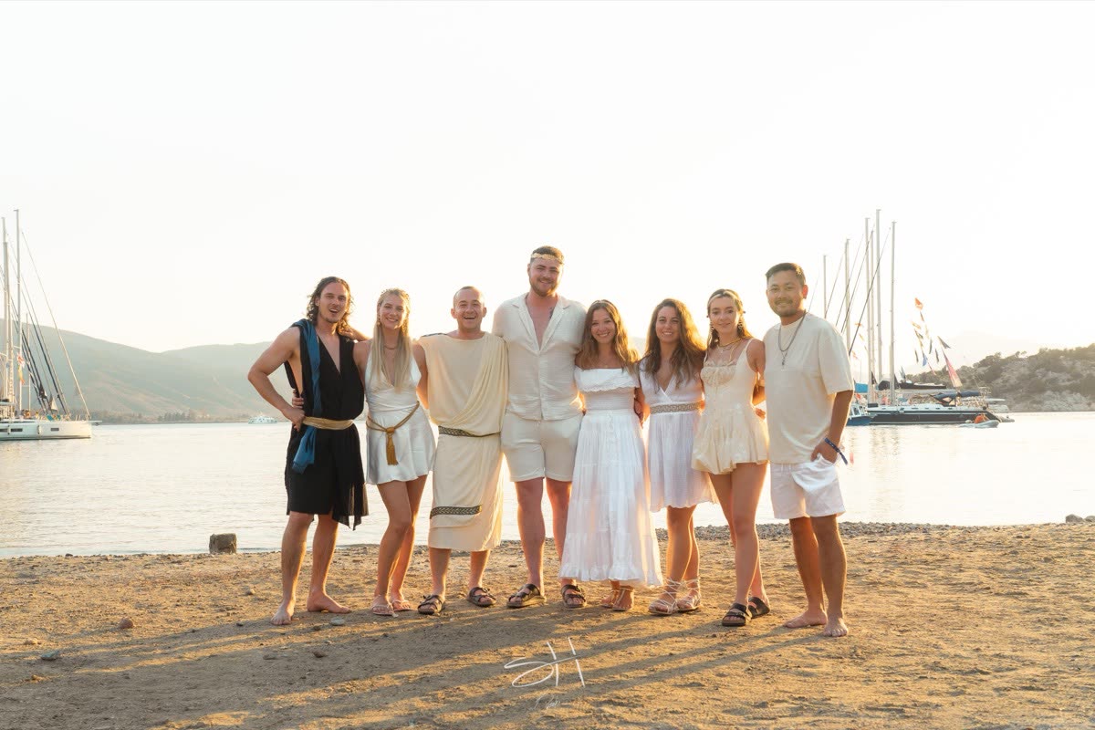 The group dressed in white and cream posing on a beach in golden evening light