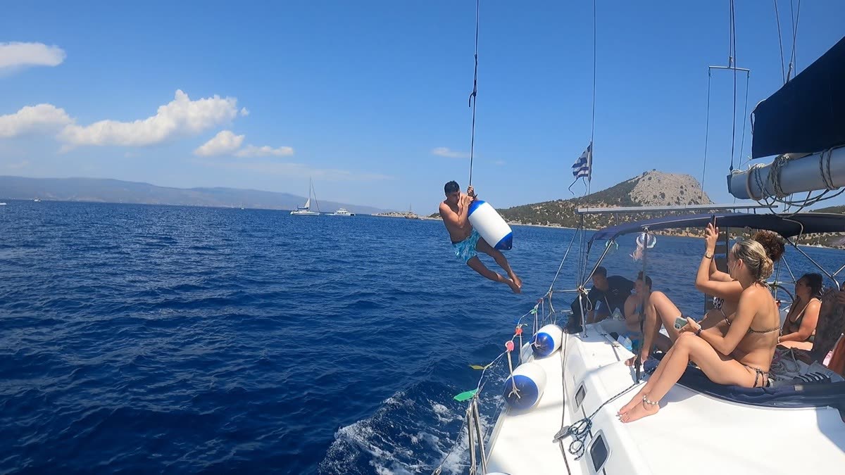 Someone jumping off the side of a yacht into deep blue water while others sit on deck