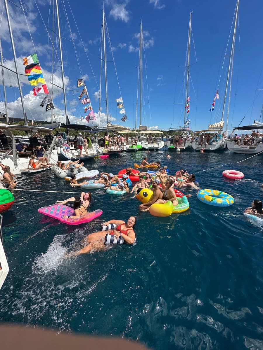 Yachts rafted together with bunting between the masts, people floating on inflatables alongside