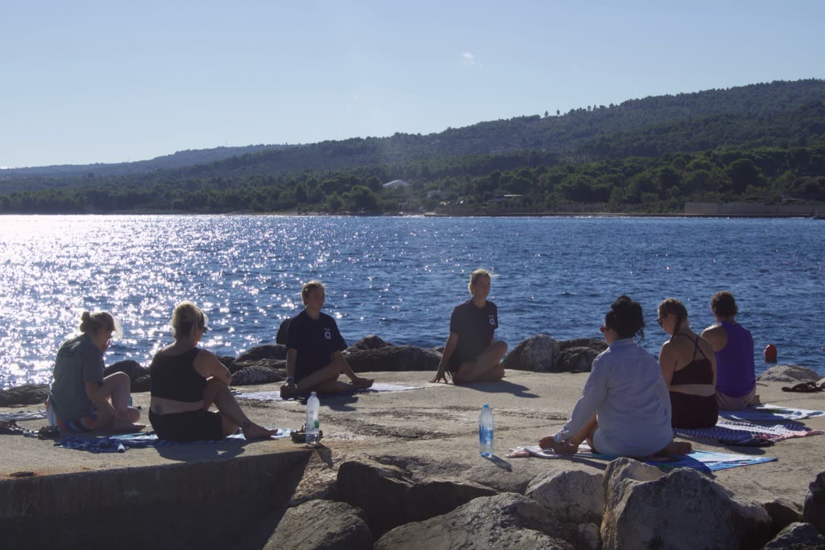 People sitting on rocks at the water's edge watching the sun on the sea