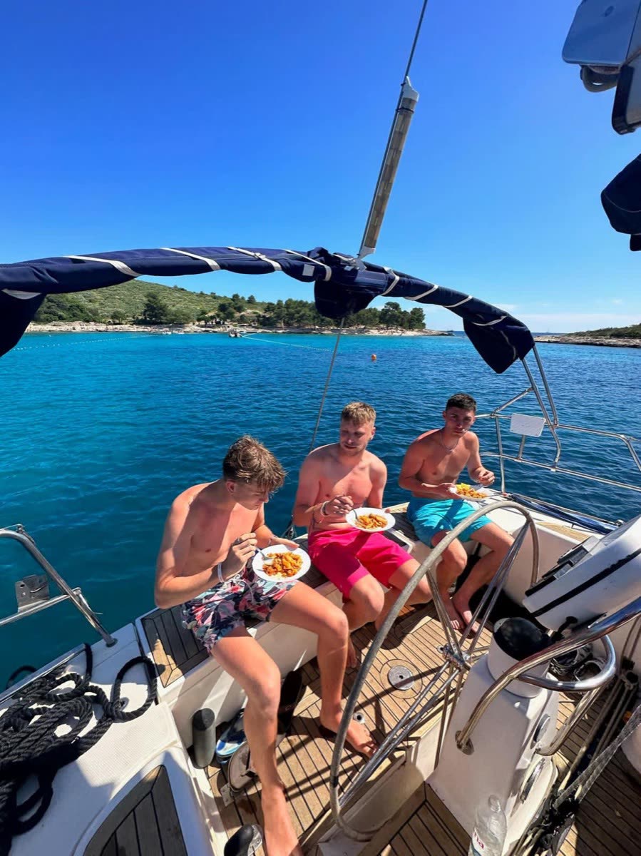 Three men eating on the foredeck of a yacht with a blue bay behind them