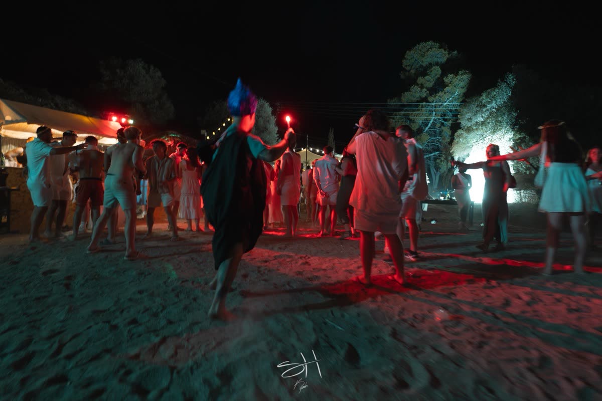 A beach party after dark, people dancing under coloured lights