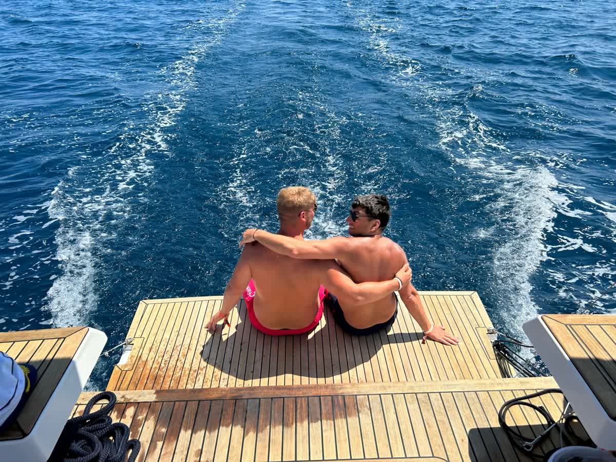 Two people sitting on the back platform of a yacht watching the wake trail behind