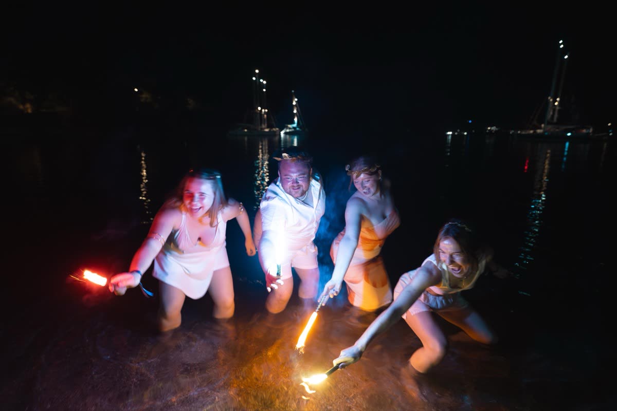 Four people standing in shallow water at night holding lit flares