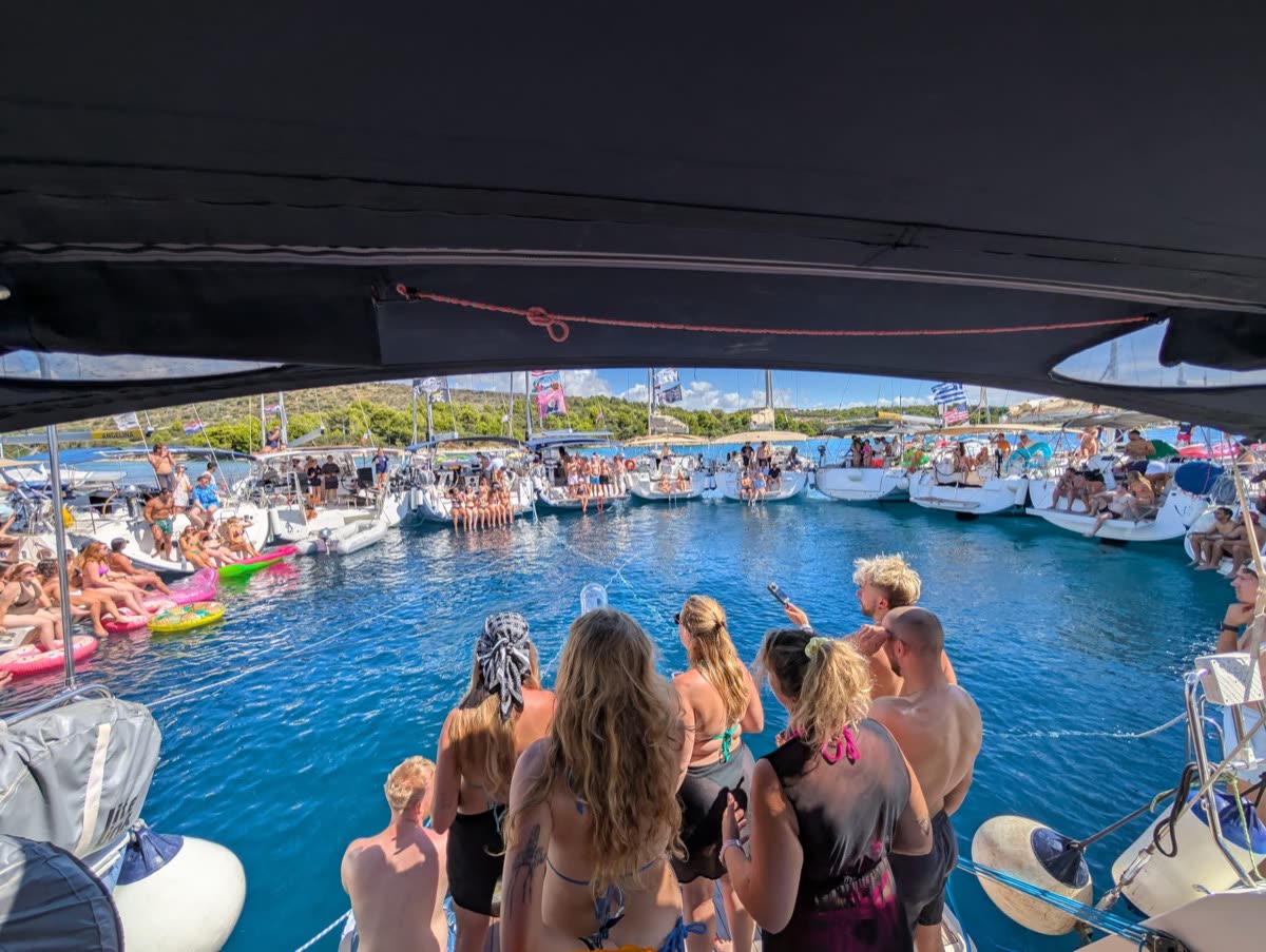 Seen from under the boom, a crowd of people in the water between rafted yachts