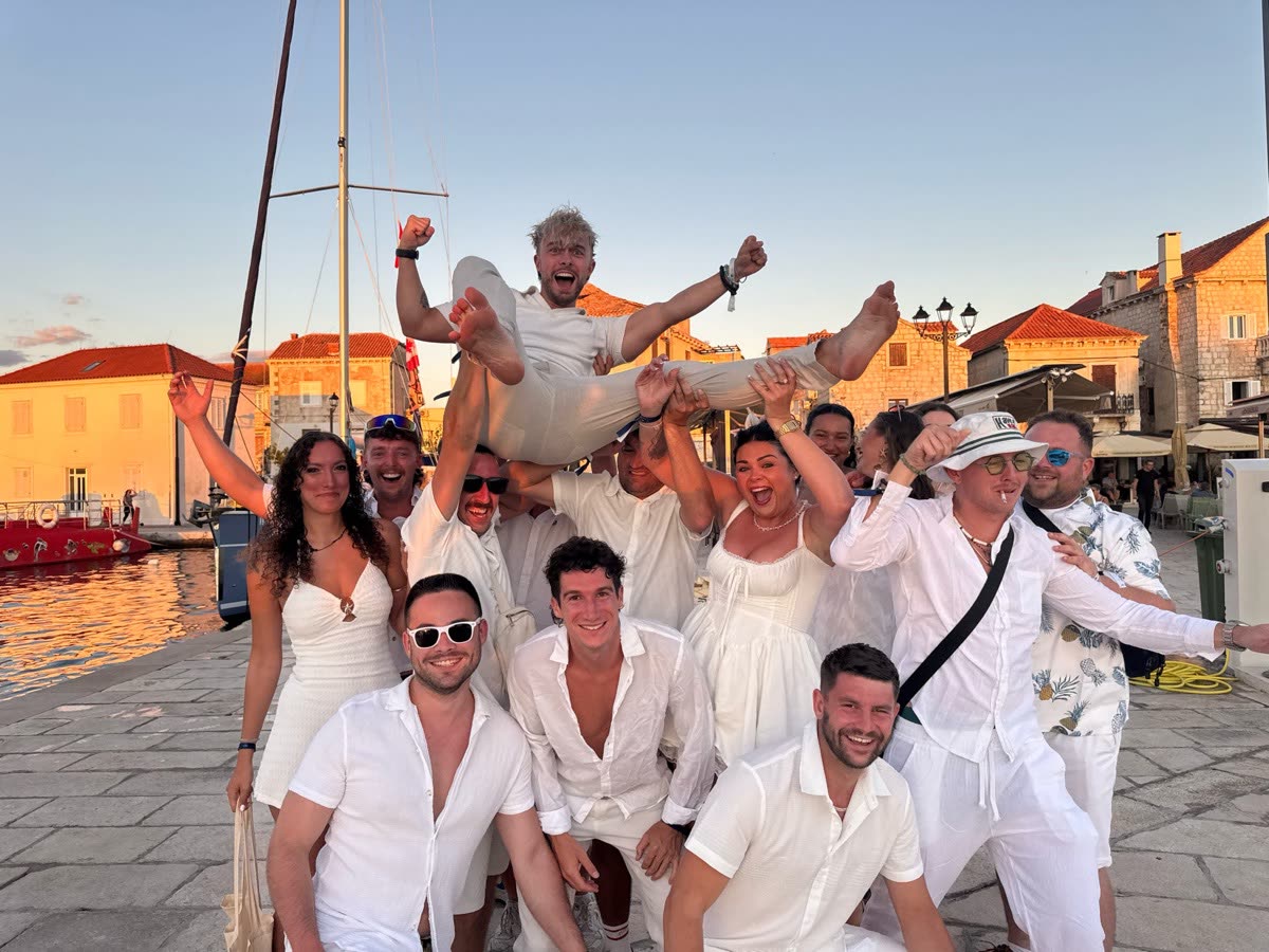 The group dressed in white on a harbour front, one person lifted up on the others' shoulders