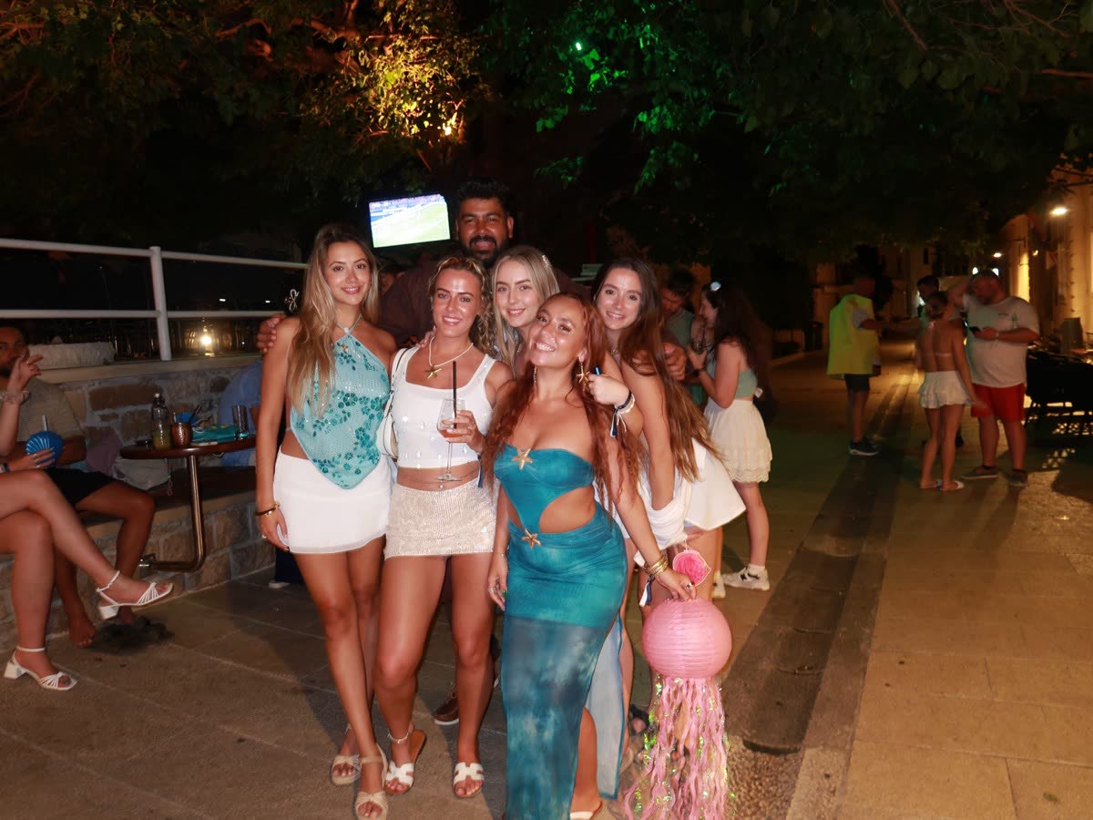 Five people posing together at an outdoor bar at night