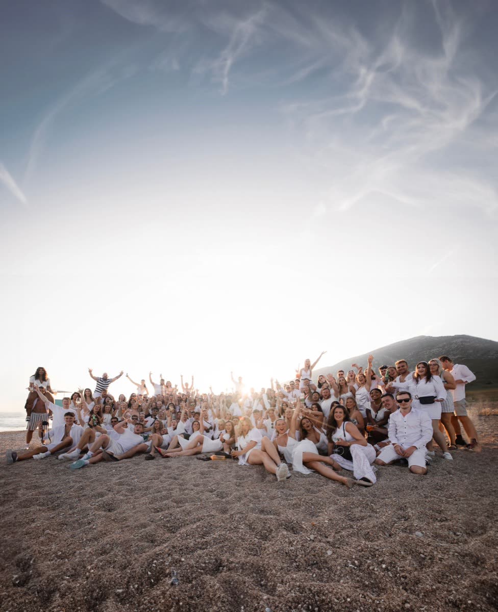 The whole group sitting together on a beach at sunset with their arms in the air