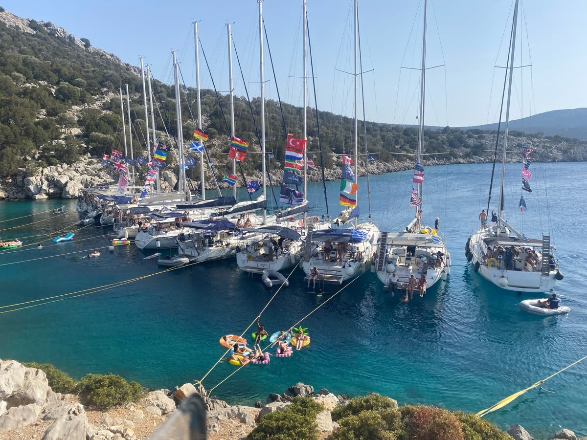 A line of yachts moored along a bay with flags and bunting strung between the masts