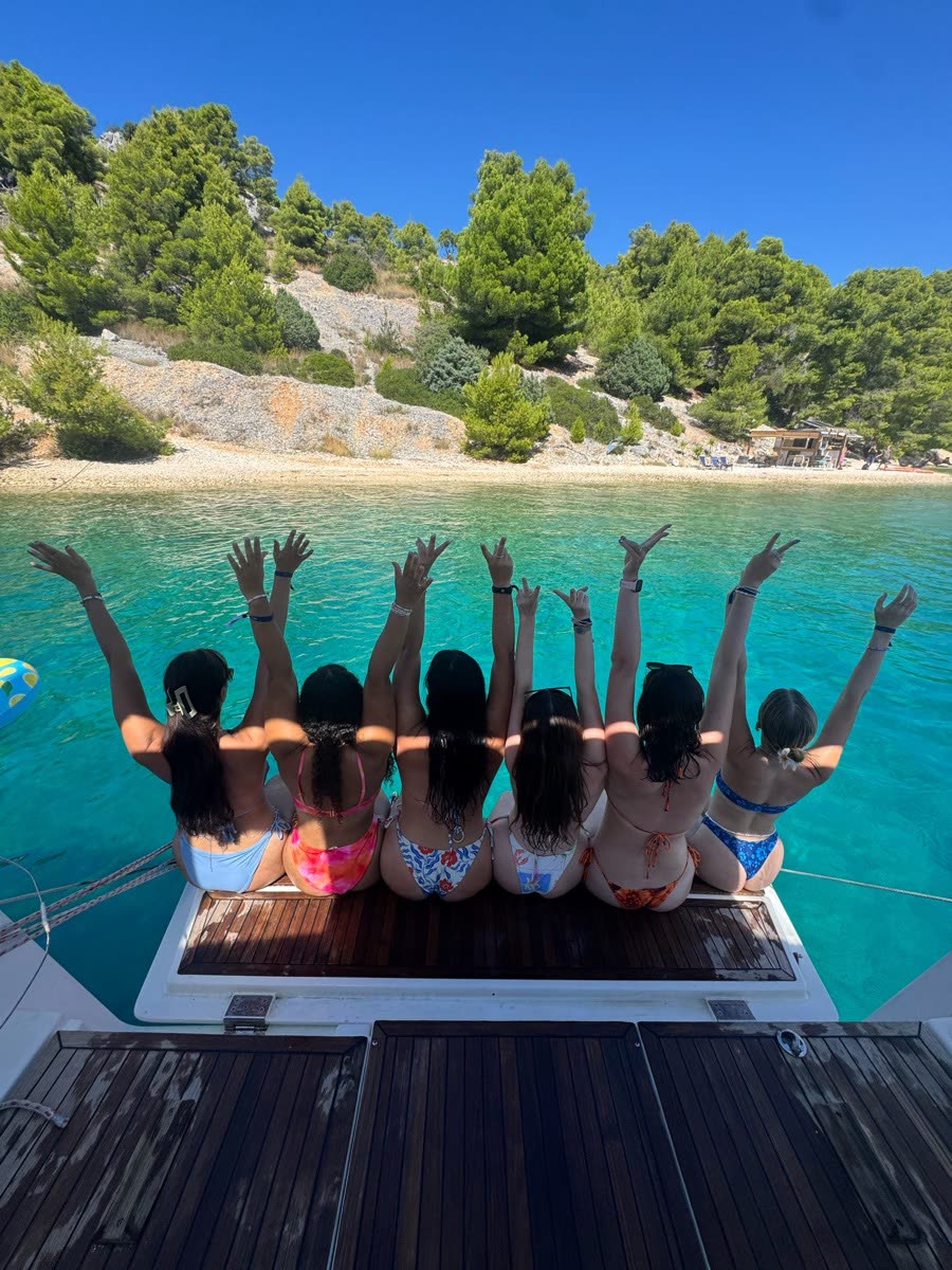 A row of people sitting along the back of a yacht with their arms raised, looking into a green bay