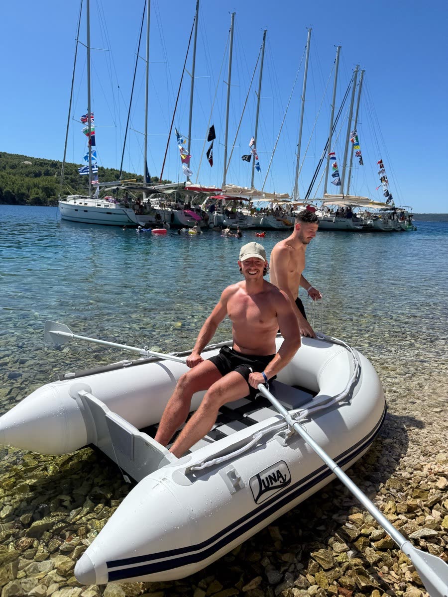 An inflatable dinghy pulled up on a pebble shore with the fleet moored behind
