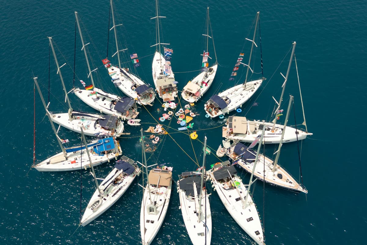 Yachts rafted together in a circle seen from above, bows pointing outwards into deep blue water