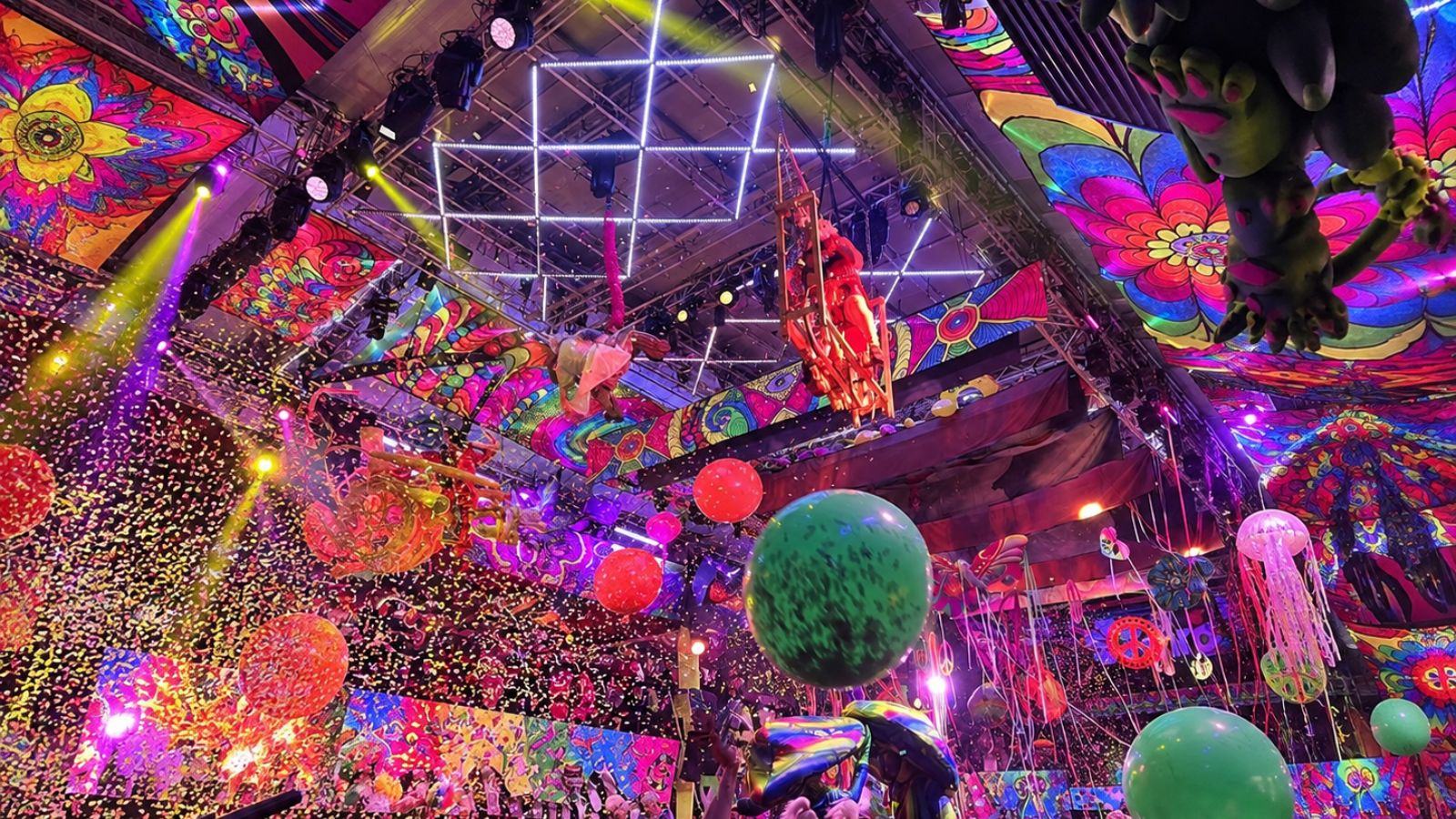 Aerial performers suspended above the crowd with confetti falling under a brightly painted ceiling