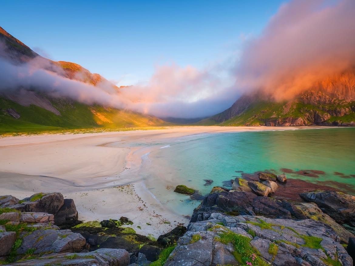 White sand and turquoise shallows with cloud spilling over the mountains