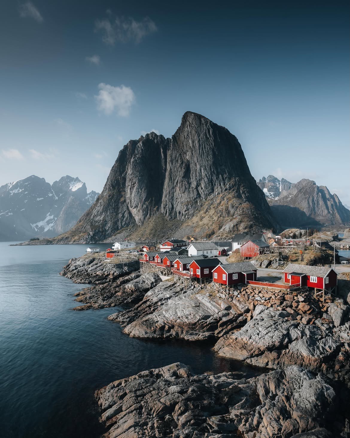 Red fishing cabins on the rocks at Hamnøy beneath a vast mountain face