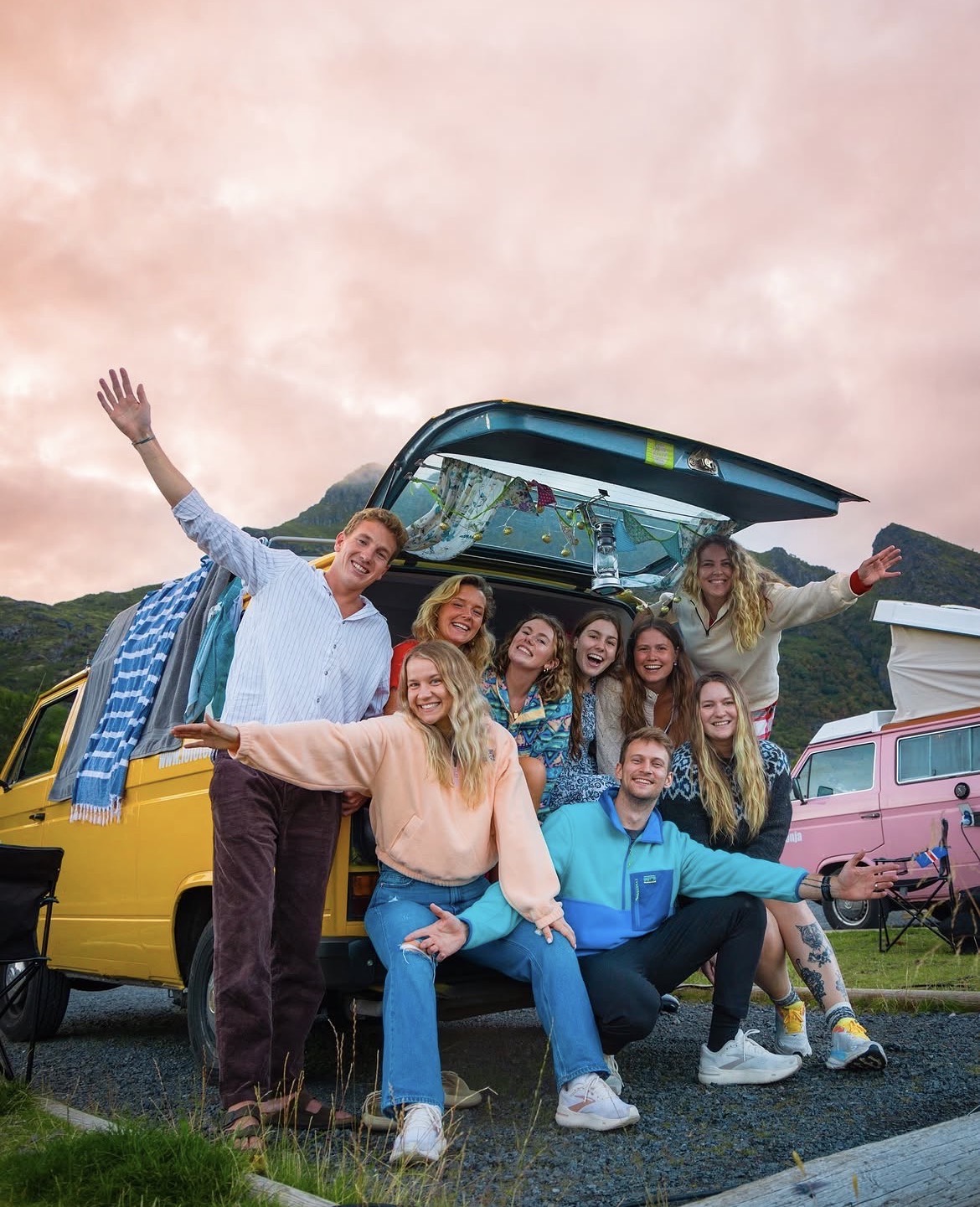 Nine people gathered round the open tailgate of a yellow camper