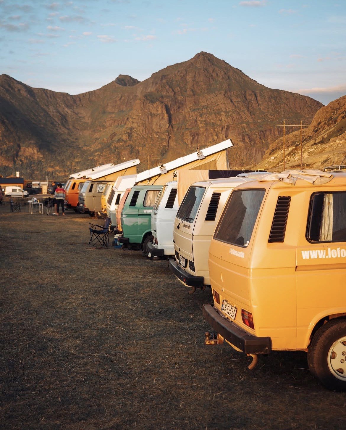 A row of campers with their pop tops raised on a campsite field