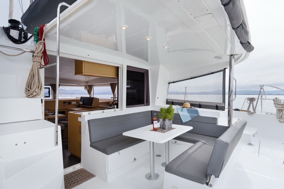 The outside seating area of a catamaran, a table and bench seating under the cockpit roof looking out to sea