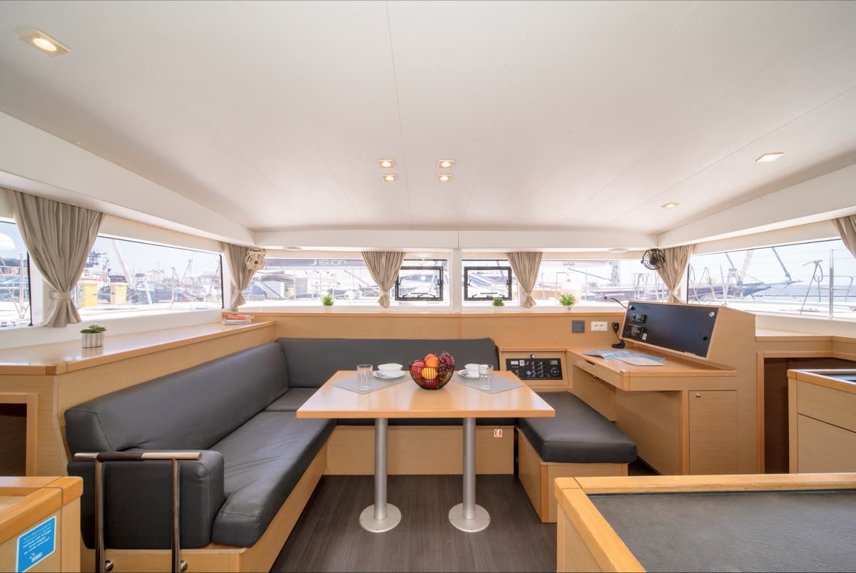 The saloon of a catamaran, a long dining table with bench seating and wide windows on both sides
