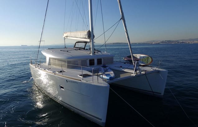 A catamaran at anchor on calm water, both hulls and the raised coachroof seen from the bow quarter