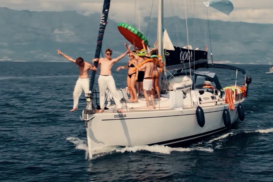 A yacht under sail with the group standing on the bow, mountains behind