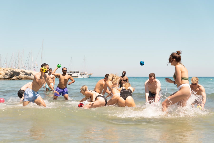 Water volleyball in the shallows, two balls in the air and a yacht moored offshore