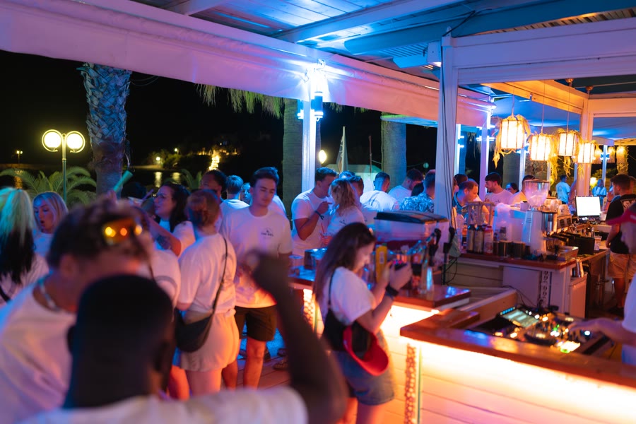 A crowded open air bar at night, lit blue and orange