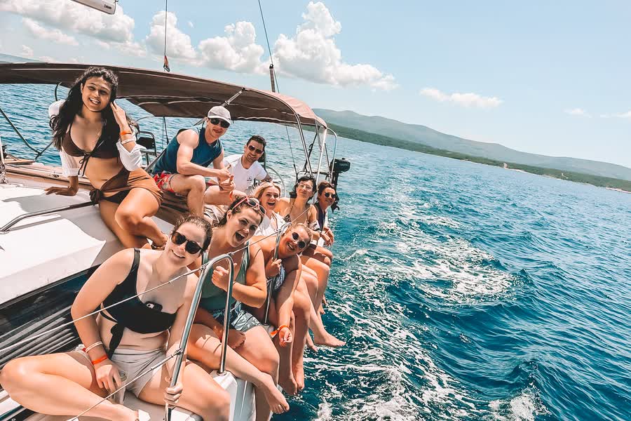 The group sitting along the side deck as the boat sails, wake running past