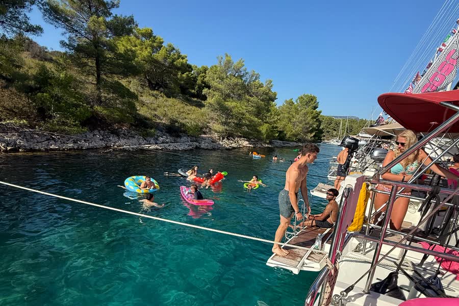 Swimmers and inflatables in a clear bay, seen down the side of a moored yacht