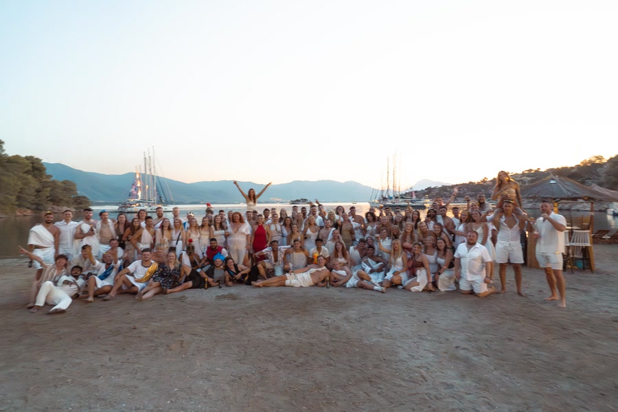 The whole group in togas on the beach at dusk, the fleet anchored behind