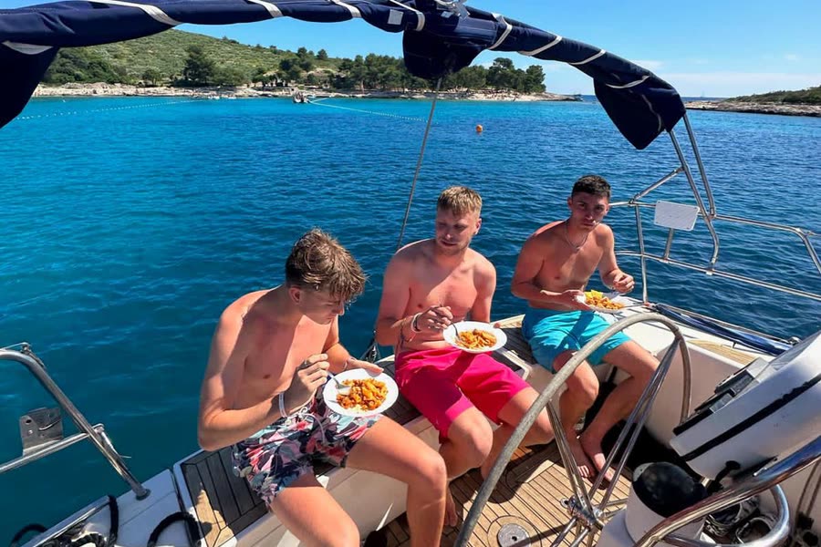 Three men eating lunch on the foredeck at anchor, a wooded island behind