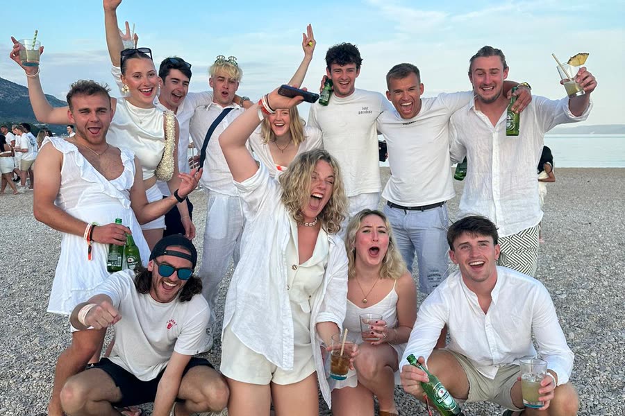 The group dressed in white on a pebble beach, drinks up
