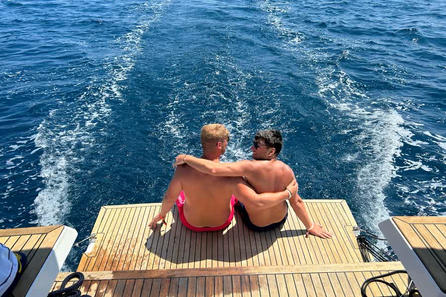Two people sitting on the stern platform watching the wake