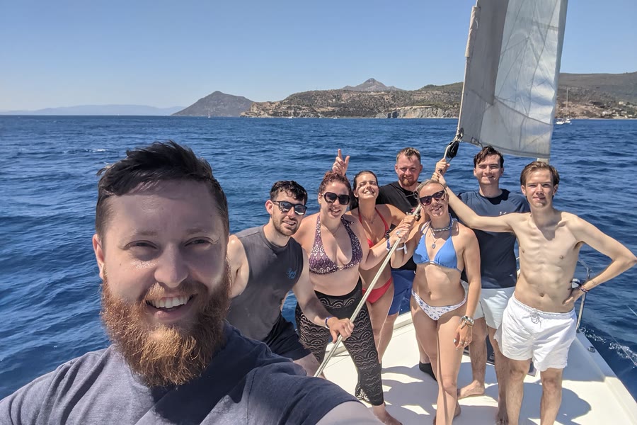 A group selfie on the foredeck under sail, an island astern