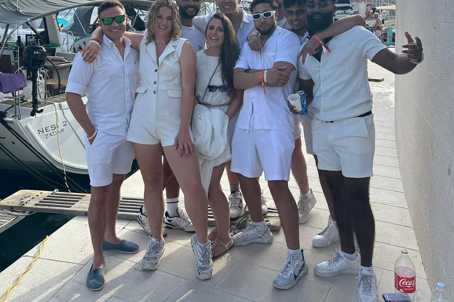 The group dressed in white on the pontoon, moored yachts and masts behind them
