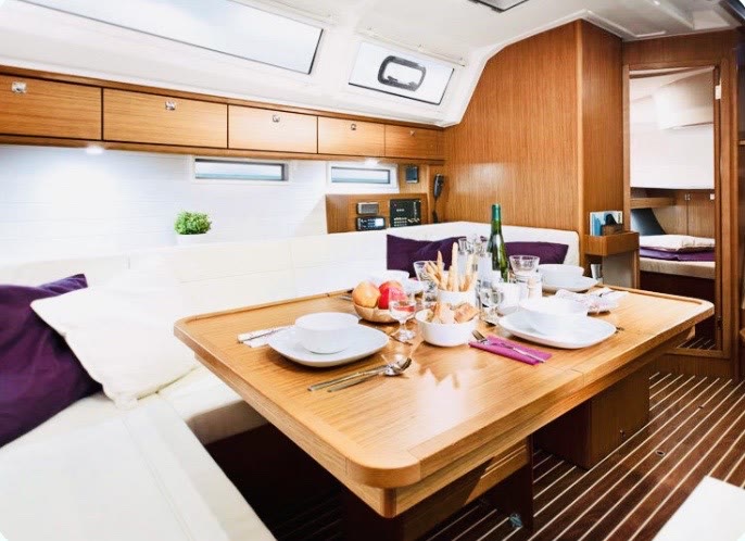The saloon of an upgraded yacht, light wood and cream seating with the table set for dinner